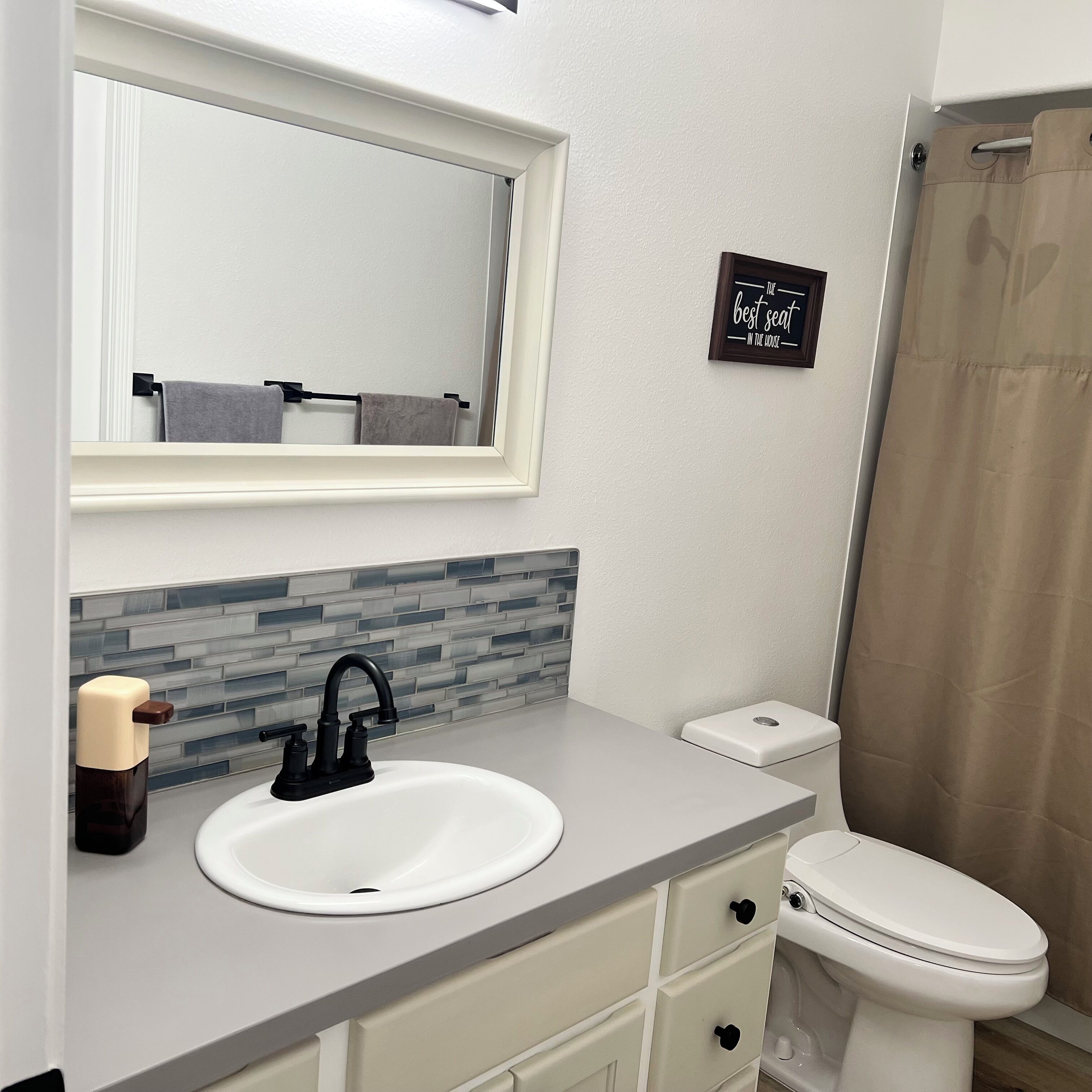 Un baño con lavamanos blanco, espejo, toallero, inodoro y cortina de ducha.