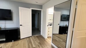 Una habitación con piso de madera, un televisor montado en la pared, un aparador y un espejo grande.
