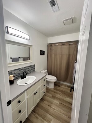 A modern bathroom with a white sink, a mirror, a toilet, and a shower curtain.
