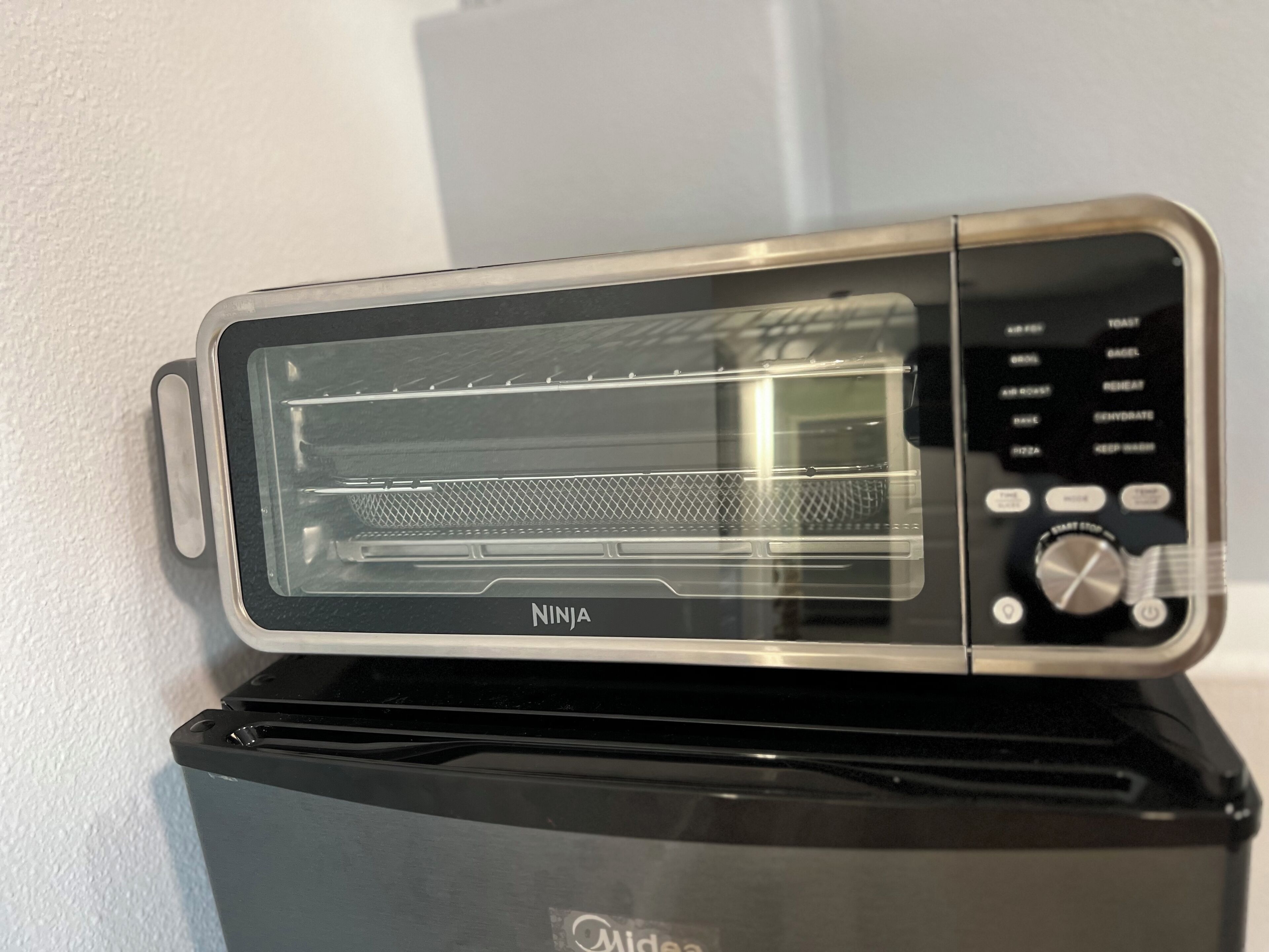 A Ninja toaster oven with a digital control panel, placed on a black appliance.