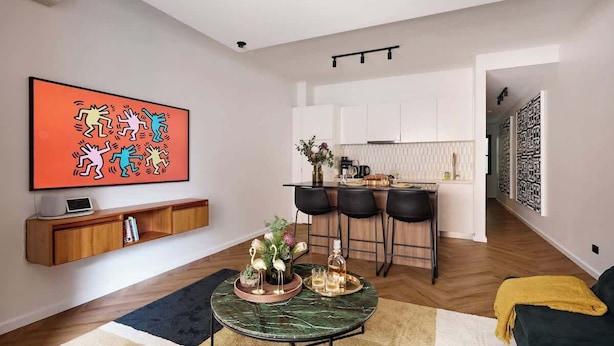 Una sala moderna con una mesa de centro de mármol, un televisor montado en la pared y una zona de cocina con barra.