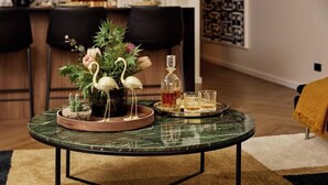 Una mesa redonda con cubierta de mármol verde, un centro de mesa floral, una botella y vasos sobre una bandeja.