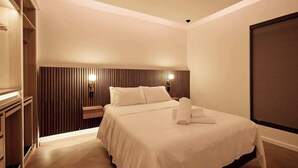 Una habitación de hotel moderna con una cama grande, cabecera de madera, lámparas de noche y una ventana con persianas.