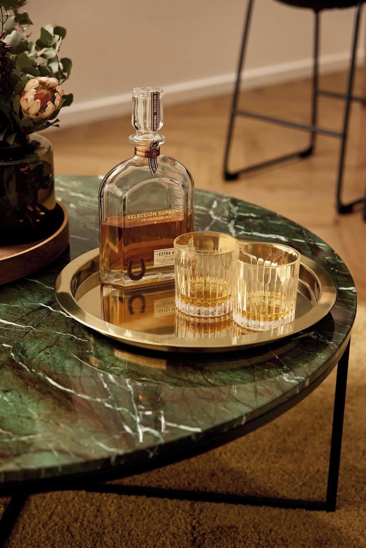 A bottle of Sección Suprema de Herradura on a tray with two glasses on a marble table.