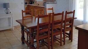 A spacious kitchen with wooden cabinets, a dining table with chairs, and a hanging light fixture. - House Des 3 filles in cantal 15700 (Ally)