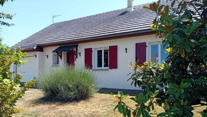 A house with a sloped roof, red shutters, and a small garden area with various plants. - House Des 3 filles in cantal 15700 (Ally)