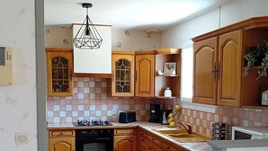 A kitchen with wooden cabinets, a gas stove, an oven, a sink, and a ceiling light fixture. - House Des 3 filles in cantal 15700 (Ally)