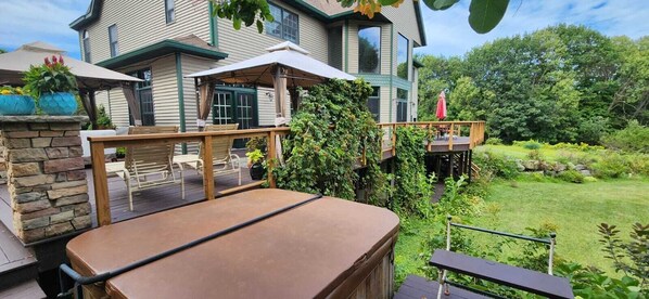 Une maison à deux étages dotée d’une terrasse, de mobilier d’extérieur et d’un jacuzzi.