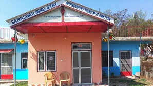 Un pequeño edificio con un cartel que dice 'SARASWATI HOME STAY' y 'APROBADO POR TURISMO Y AVIACIÓN'.