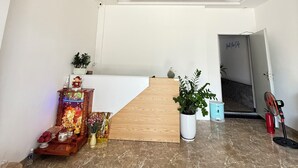 A modern interior with a wooden reception desk, a potted plant, a red ceiling light, and a marble floor. - Lavi home (Da Nang)