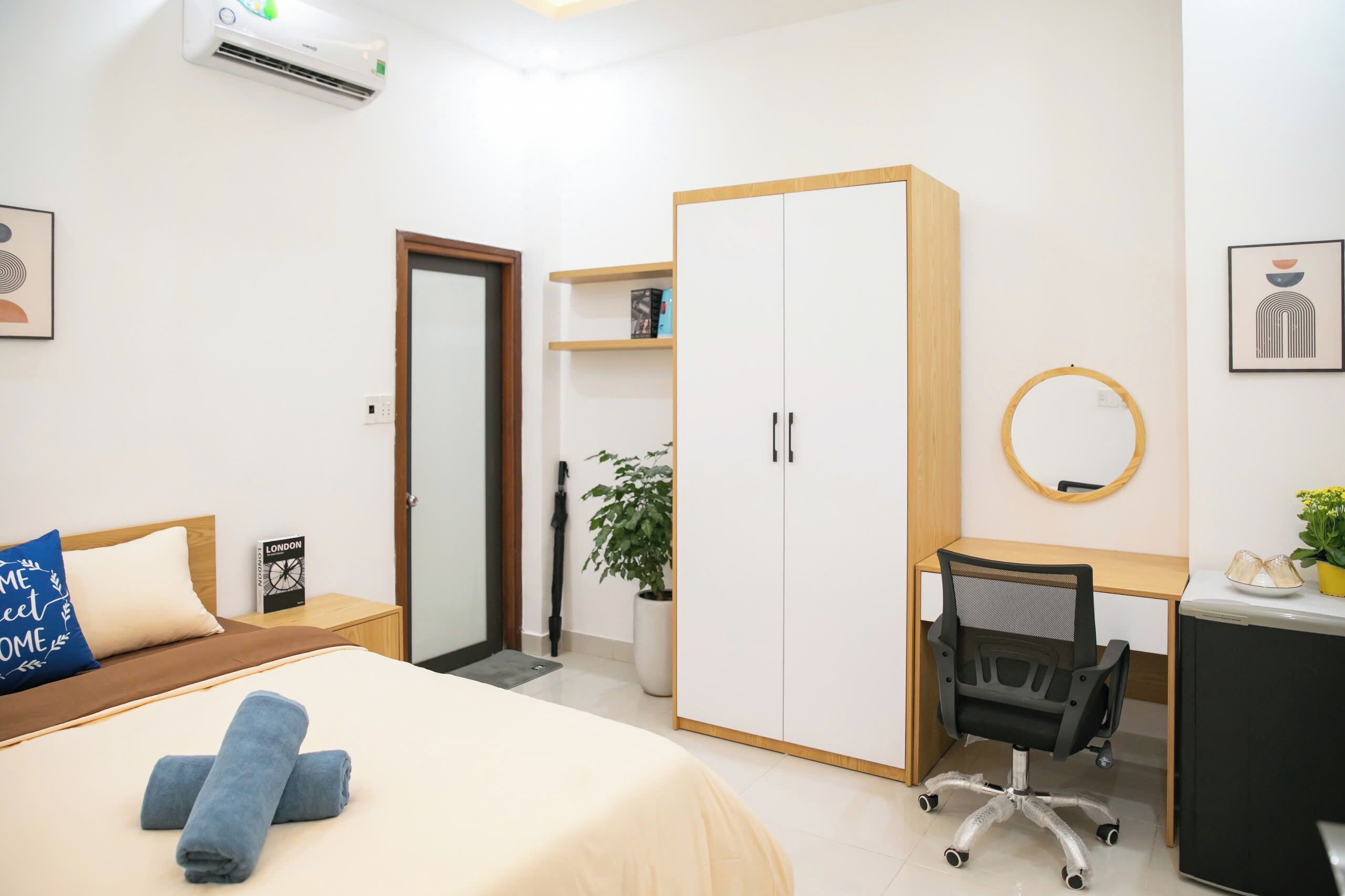 A hotel room with a bed, a desk, a wardrobe, and a potted plant.