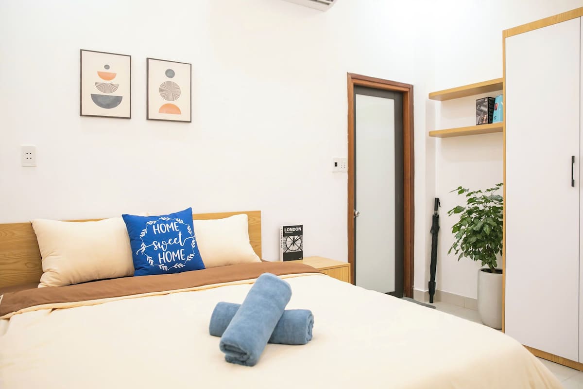 A neatly made bed with a blue pillow, a pair of rolled towels, and a book titled "LONDON" on the nightstand.