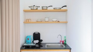 A compact kitchen with a sink, a kettle, and a coffee maker on the counter. There are shelves above the counter holding pots and bowls. - Lavi home (Da Nang)
