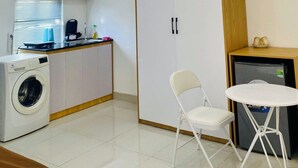 A compact kitchen with a washing machine, a small dining table with a chair, and a cabinet with two doors. - Lavi home (Da Nang)