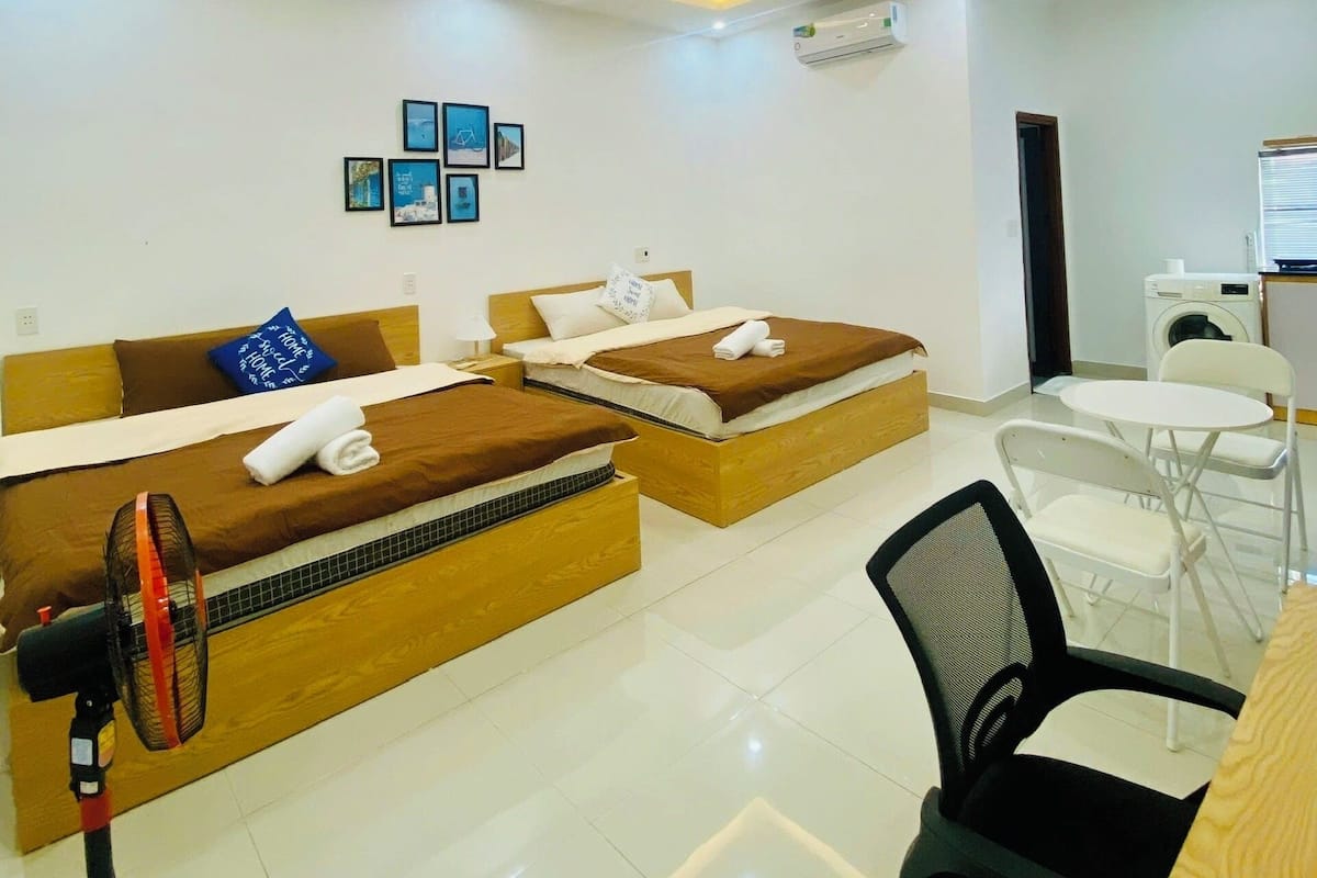 A hotel room with two beds, a desk, a chair, and a washing machine.