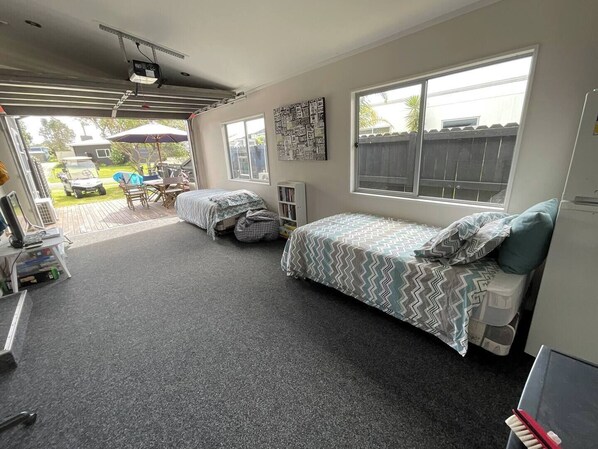 A compact room with two single beds, a small desk, and a chair. There is a window providing a view of the outside.
