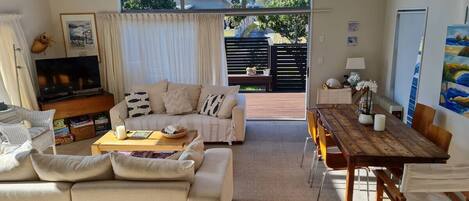A spacious living room with a sofa, coffee table, and dining table. There is a large window providing a view of the outdoors.