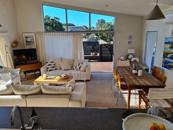 A spacious living room with a sofa, coffee table, and dining table. There is a large window providing a view of the outdoors.