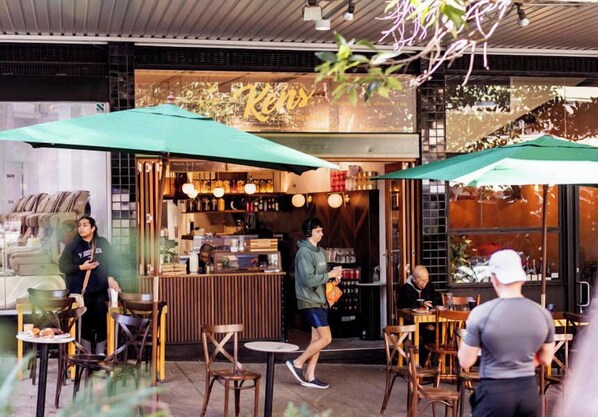 Un café en plein air avec des tables et des chaises, un comptoir où figure le menu, et des parasols pour faire de l’ombre.