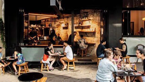 An outdoor seating area with tables and chairs, a bar area with stools, and a brick wall interior. - Light Filled 1BR  Retreat with Car Park & Pool (Elizabeth Bay)