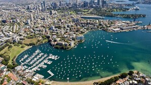 An aerial view of a city with a marina filled with boats, surrounded by high-rise buildings and a large body of water. - Light Filled 1BR  Retreat with Car Park & Pool (Elizabeth Bay)