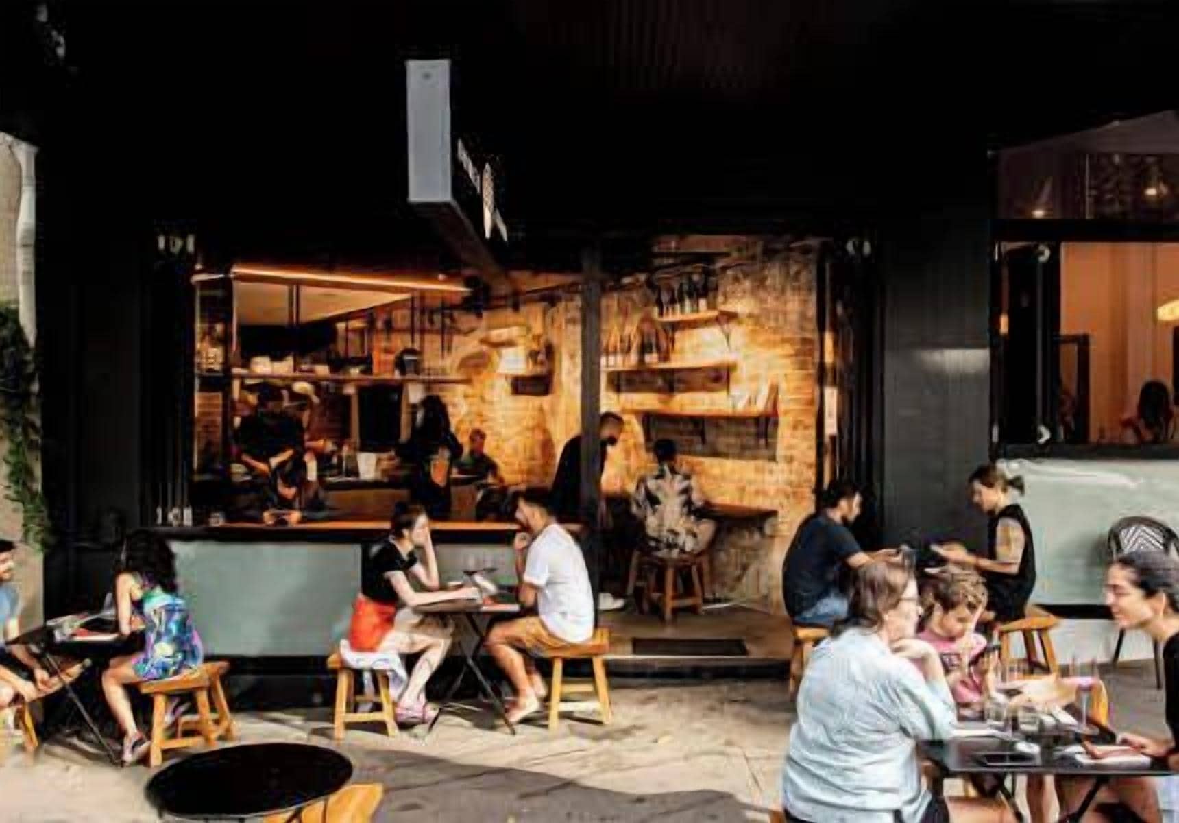 An outdoor seating area with tables and chairs, a bar area with stools, and a brick wall interior.