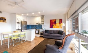 Un appartement moderne comprenant une cuisine, un coin repas et un salon. Il est doté d’une grande fenêtre, d’un canapé et d’un fauteuil.