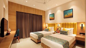 A hotel room with two beds, a desk, a television, and a large window with curtains. - Park Residency Puthupally (Kottayam)