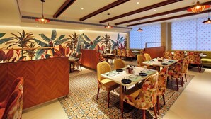 A restaurant with wooden paneling, tropical wall art, and patterned flooring. Tables are set with chairs and dining ware. - Park Residency Puthupally (Kottayam)