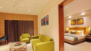 A modern hotel room with a large bed, two sofas, a round coffee table, and a wooden accent wall. - Park Residency Puthupally (Kottayam)