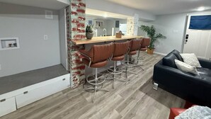 En moderne stue med en sort sofa, et spiseområde med et træbord og læderstole i brun, samt en væg med murstensdetaljer.