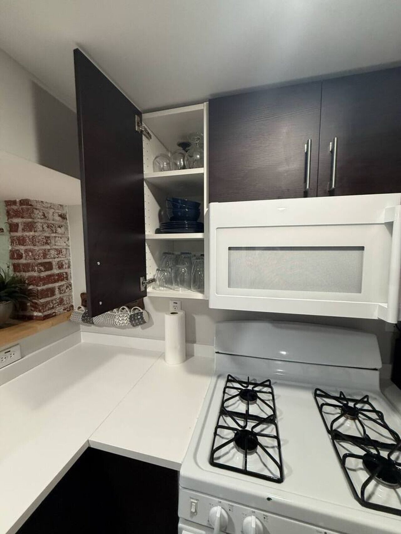 A compact kitchen with a gas stove, a microwave, and dark wooden cabinets.