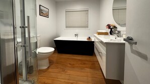Ein modernes Badezimmer mit einer Duschkabine aus Glas, einer weißen Toilette, einer schwarzen Badewanne und einem weißen Waschbecken mit Spiegel.