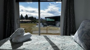 Ein Schlafzimmer mit großem Fenster, einem Bett und Blick auf eine angelegte Grünfläche mit Bäumen und einem Gebäude.