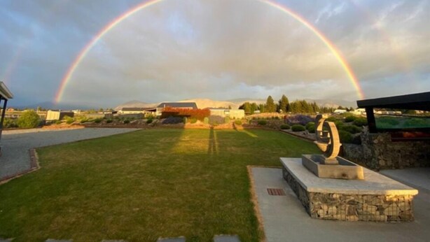Ein Park mit einer Steinstatue und einem Regenbogen im Hintergrund.