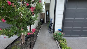 A paved pathway leading to a garage door, flanked by a flower bed and a tree with pink flowers. - Urban Nest HTX (Houston)