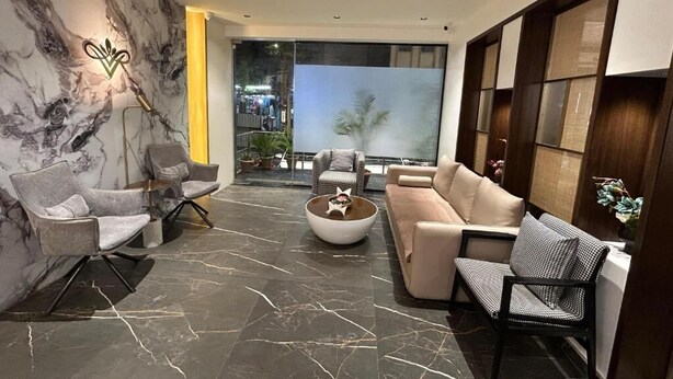 A modern living room with a marble wall, a sofa, two armchairs, a coffee table, and a view through a glass door. - HOTEL VIJAY VILAS (Jalna)