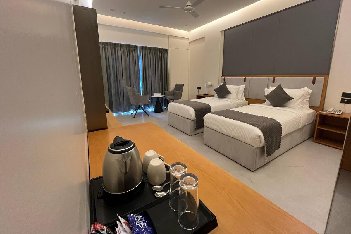 A hotel room with two beds, a desk with a kettle, cups, and a tray, and a view of the room's interior.