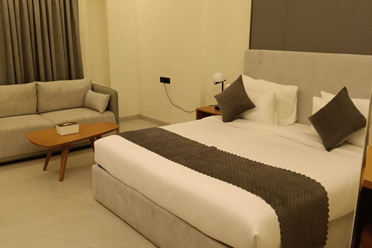 A hotel room with a bed, a sofa, a small table, and a nightstand with a lamp.