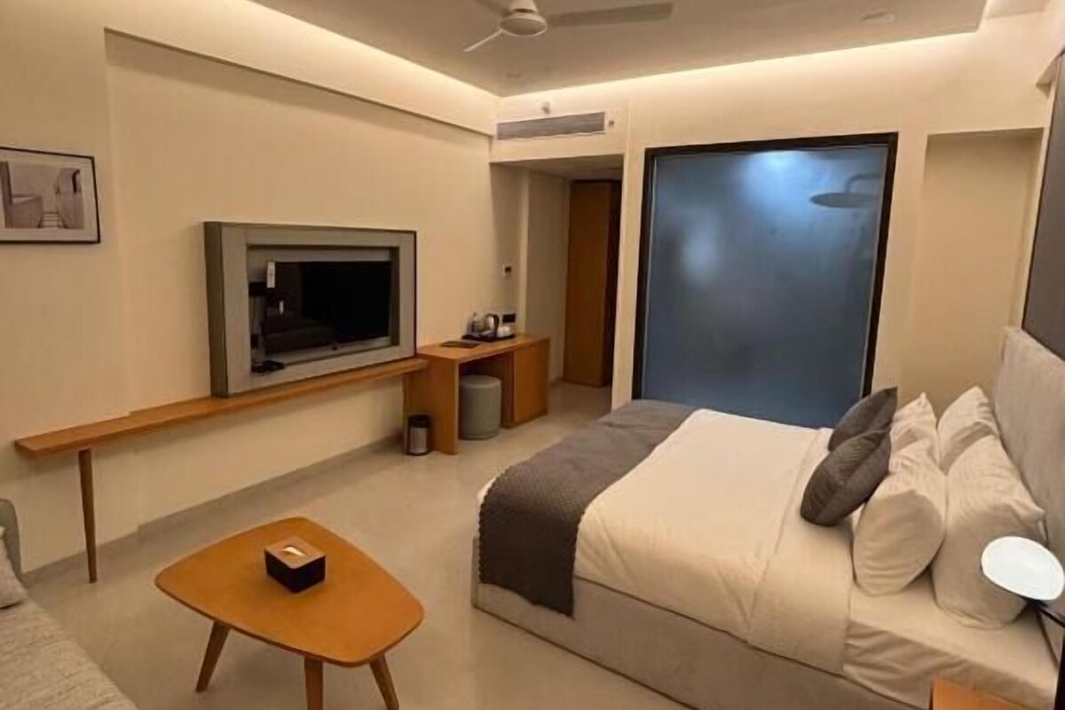 A modern hotel room with a bed, a TV, a desk, and a ceiling fan.