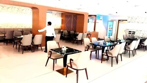 A spacious restaurant with multiple dining tables and chairs, a waiter in uniform, and a modern interior design. - HOTEL VIJAY VILAS (Jalna)