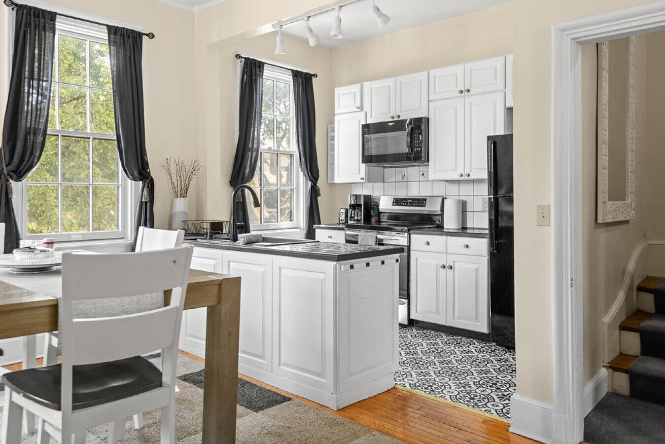 A modern kitchen with white cabinetry, a black countertop, and a black refrigerator.