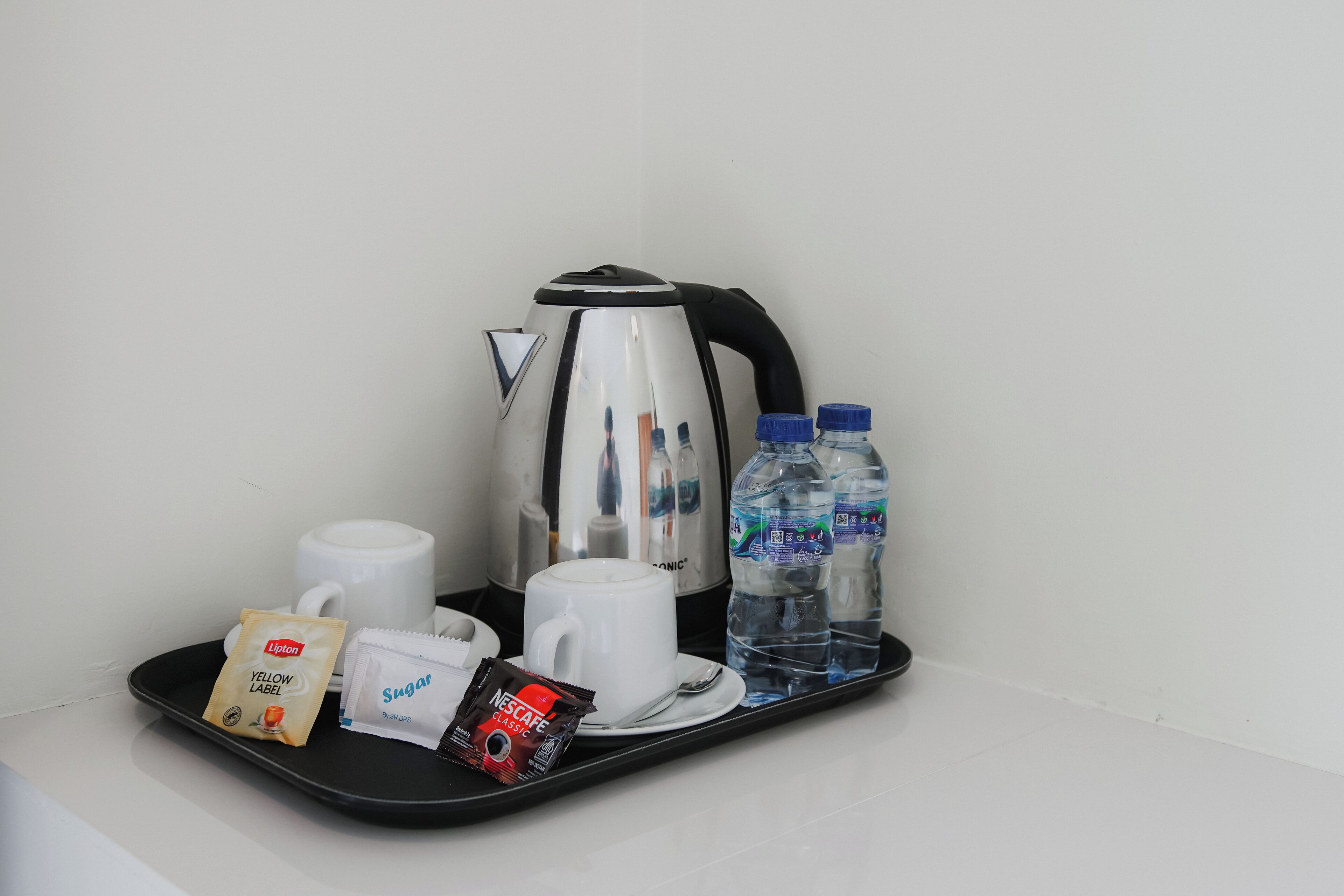 A tray with a coffee maker, two cups, Lipton tea, sugar packets, Nescafe Classic coffee, and two water bottles.