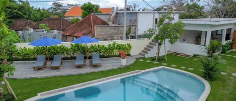 A swimming pool with lounge chairs and umbrellas, surrounded by a well-maintained lawn and a variety of plants.