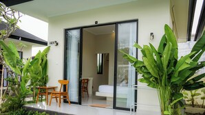 Une chambre d’hôtel moderne dotée d’une porte vitrée donnant sur un balcon, d’un lit et d’un petit coin salon avec une chaise et une table.