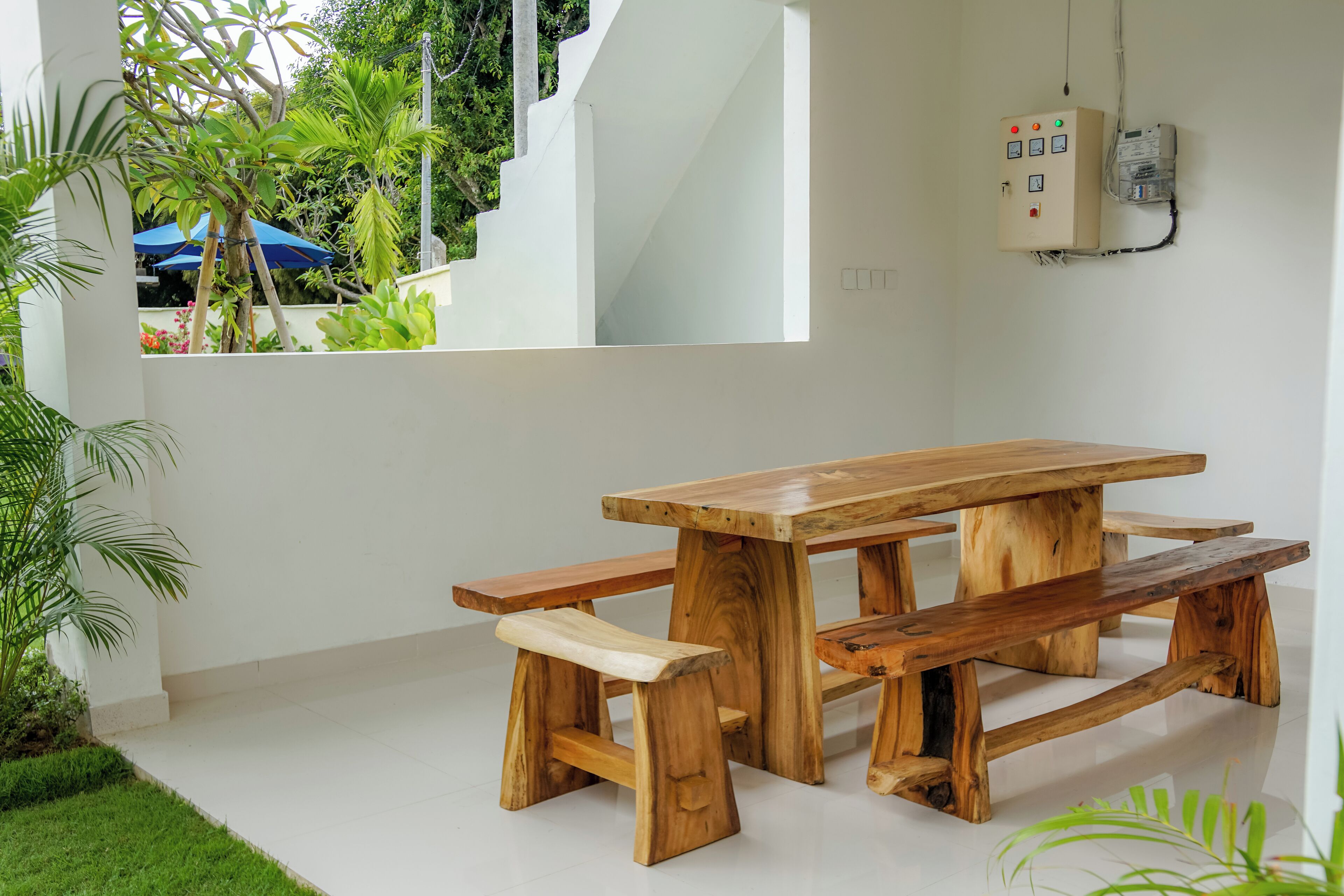 Una mesa de picnic de madera con bancos en un espacio de paredes blancas, con vista a follaje exterior.