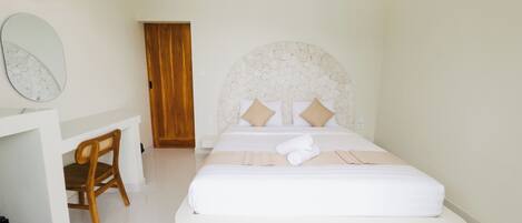 A hotel room with a bed, a wooden chair, a desk, and a stone wall.
