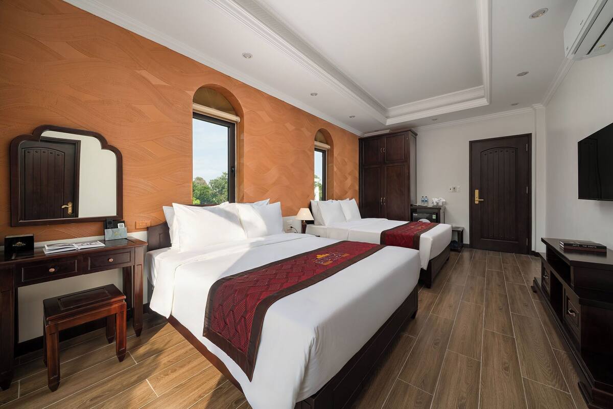 Una habitación de hotel con dos camas, un escritorio, una silla, un televisor y un armario.