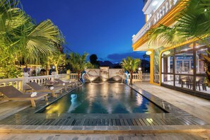 An outdoor swimming pool with lounge chairs, a stone fountain, and a view of mountains at dusk. - Tam Coc Babylon Hotel (Hoa Lu)