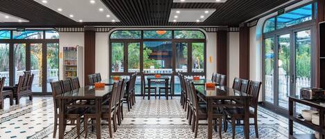 A spacious dining area with large windows, a tiled floor, and a view of a garden.